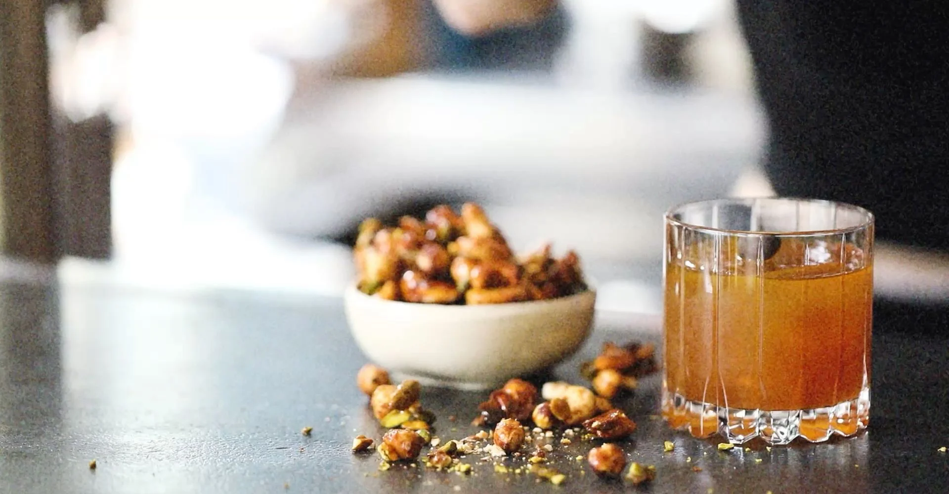 Bowl of caramelized nuts and a glass of amber drink, banner for the SHO Umami Booster page