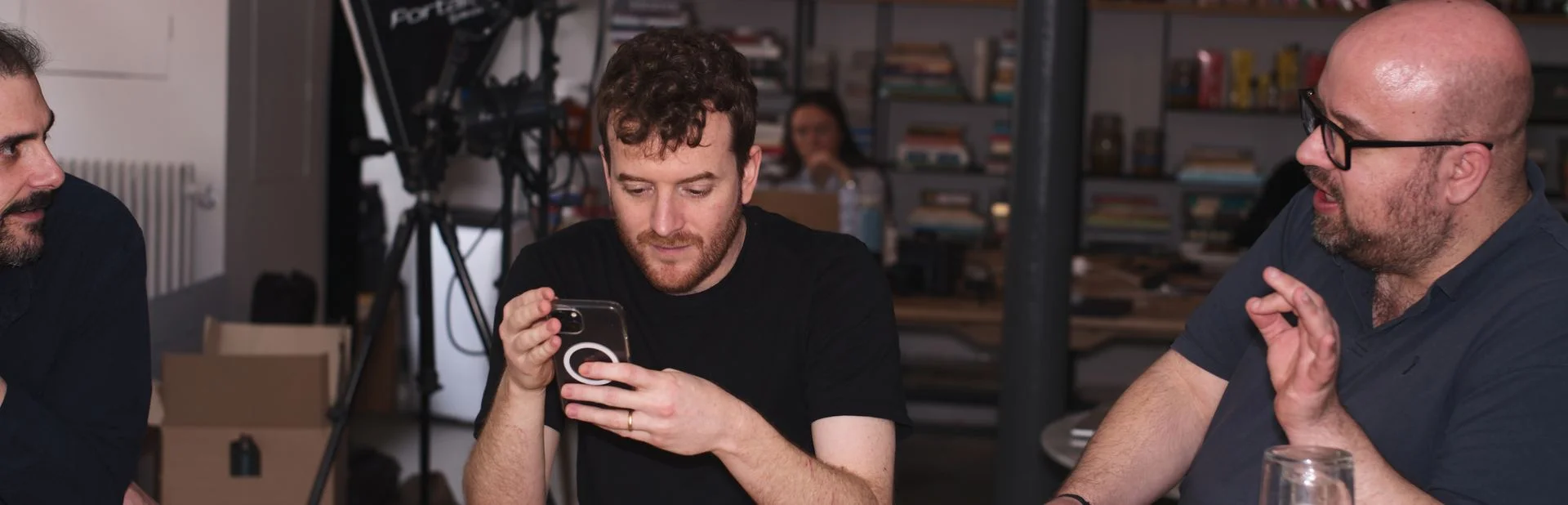 Membres de l'équipe EATTT en studio, l'un vérifiant du contenu sur son téléphone, bannière de la page Contact