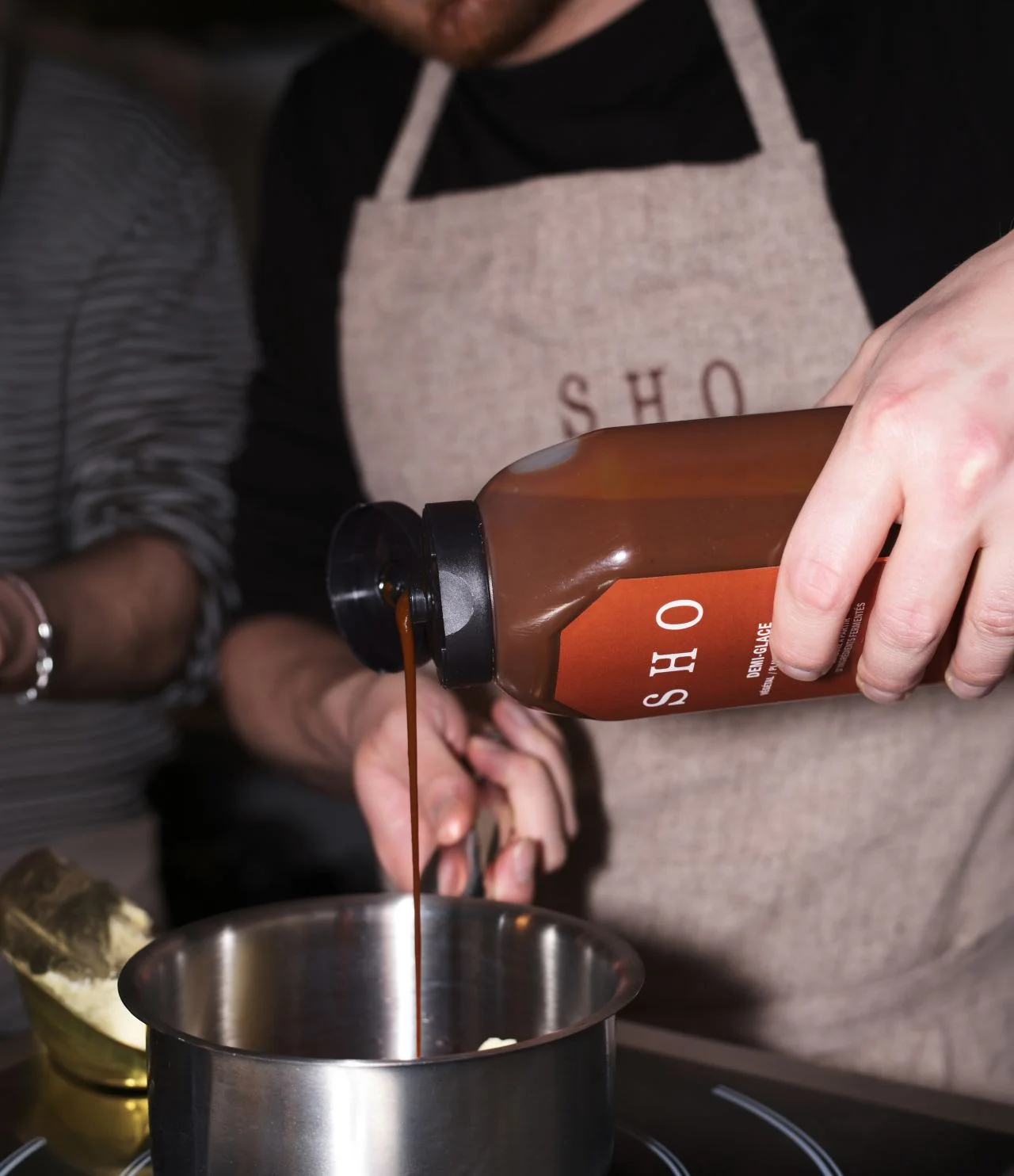 Chef pouring SHO Demi-Glace concentrate into a metal pot while cooking