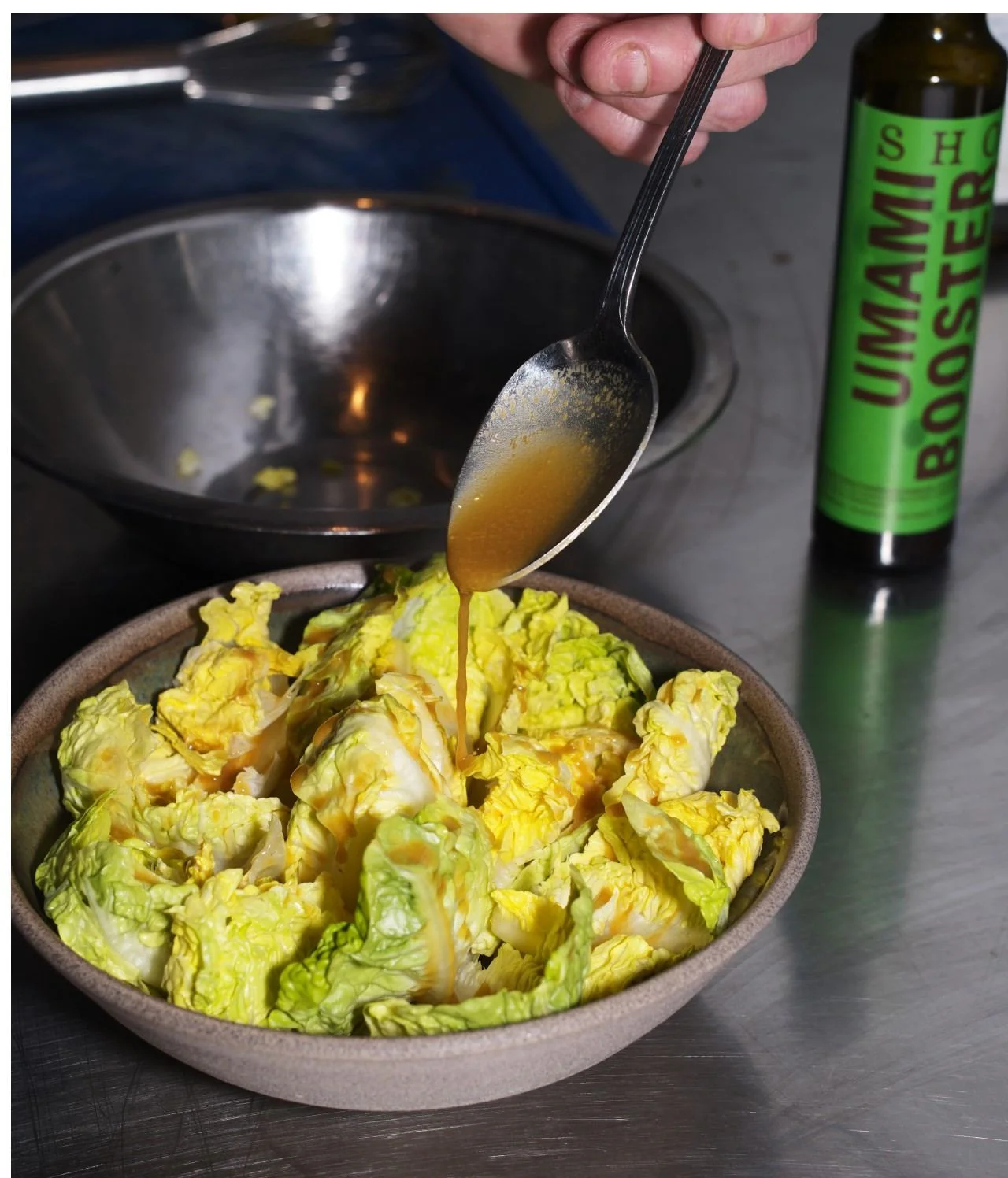 SHO Umami Booster being spooned over a bowl of fresh lettuce leaves