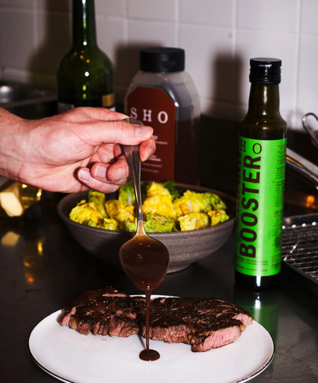 Sauce SHO Umami Booster versée sur un steak grillé avec la bouteille du produit en arrière-plan