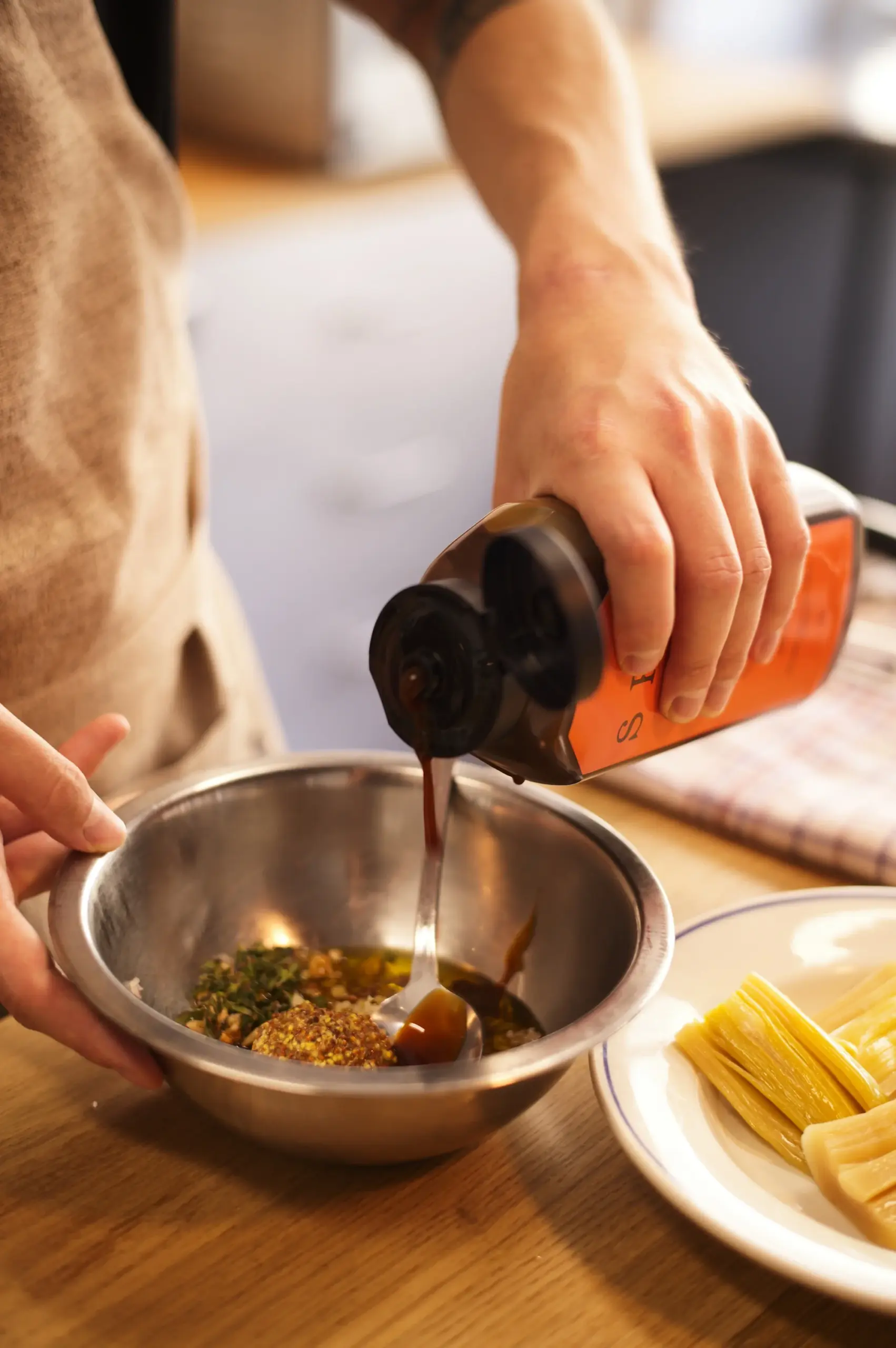 Chef pouring rich fermented liquid into a stainless steel bowl to enhance sauce depth and umami.