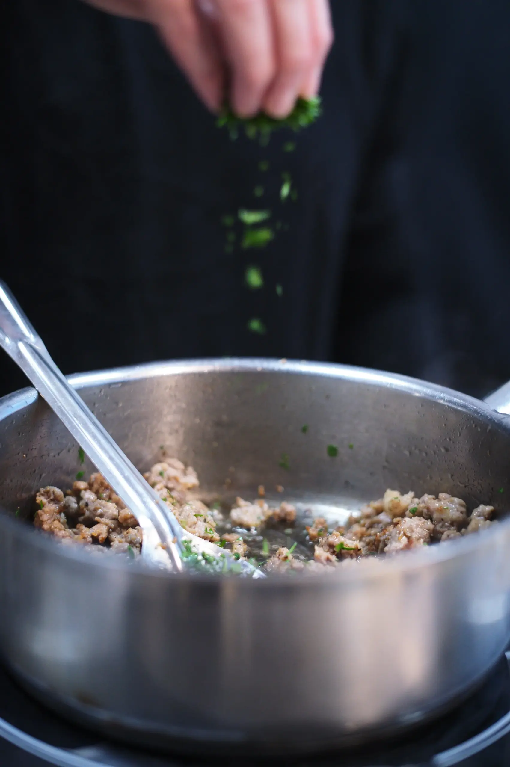 Adding fresh chopped herbs to a simmering pan of food to build culinary layers.