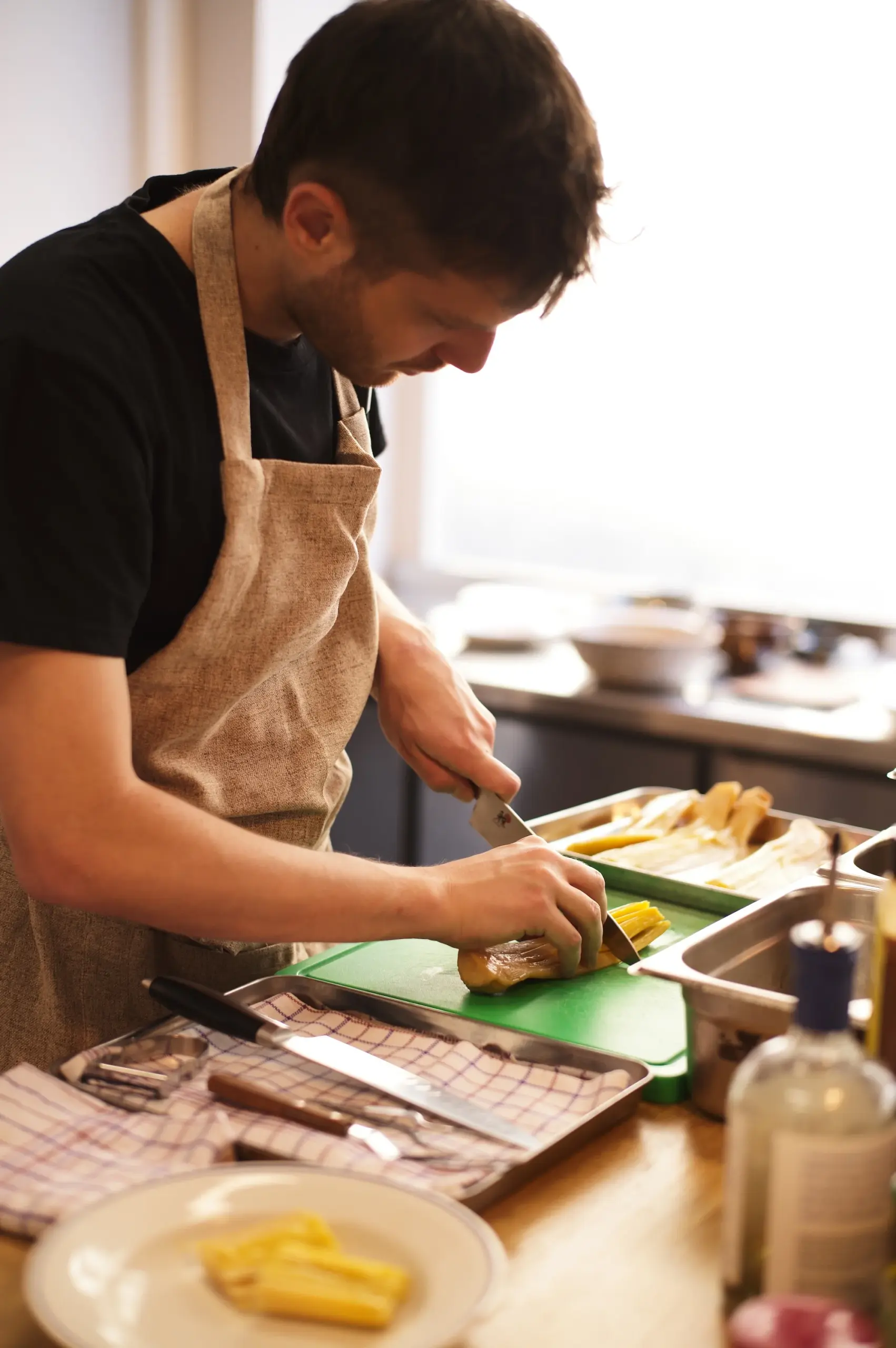 Chef découpant avec soin des légumes rôtis sur une planche à découper verte.