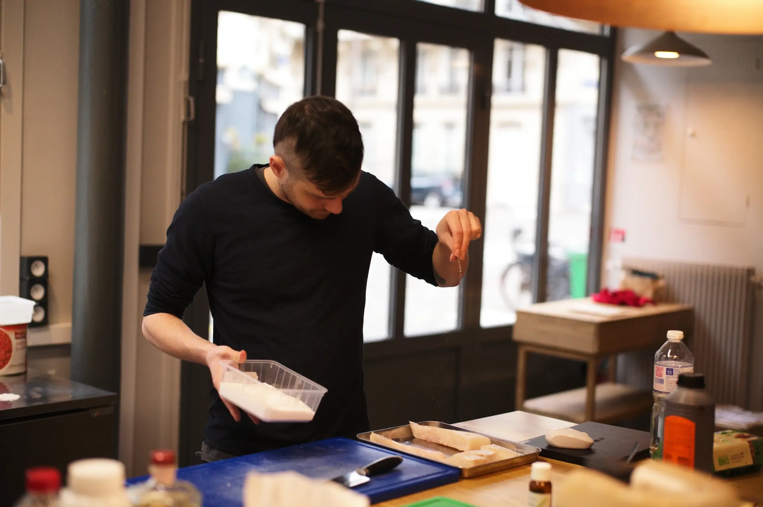 Chef seasoning raw ingredients during culinary development in a professional kitchen.