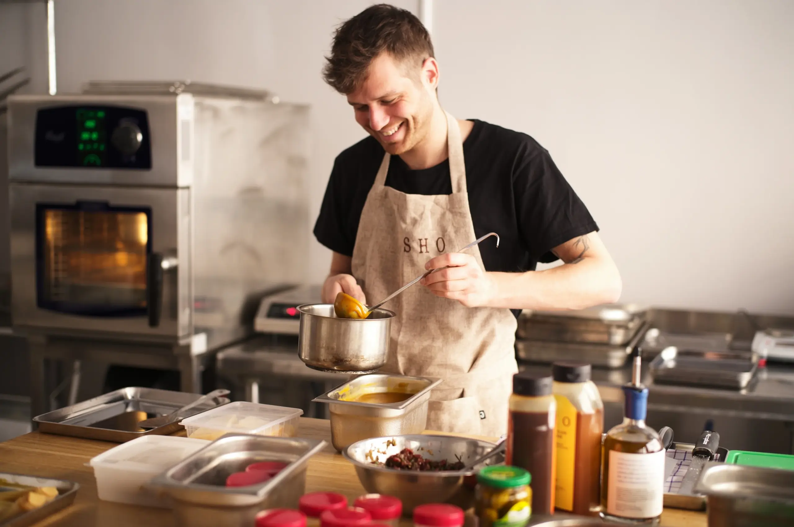 Chef en tablier versant une sauce onctueuse depuis une casserole à l'aide d'une louche.