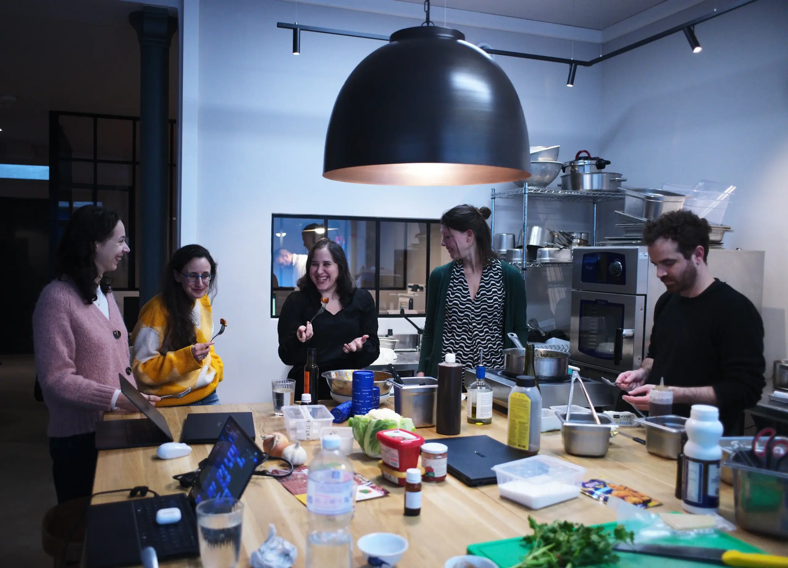 Food development team tasting and testing different recipe formulations around a kitchen counter.