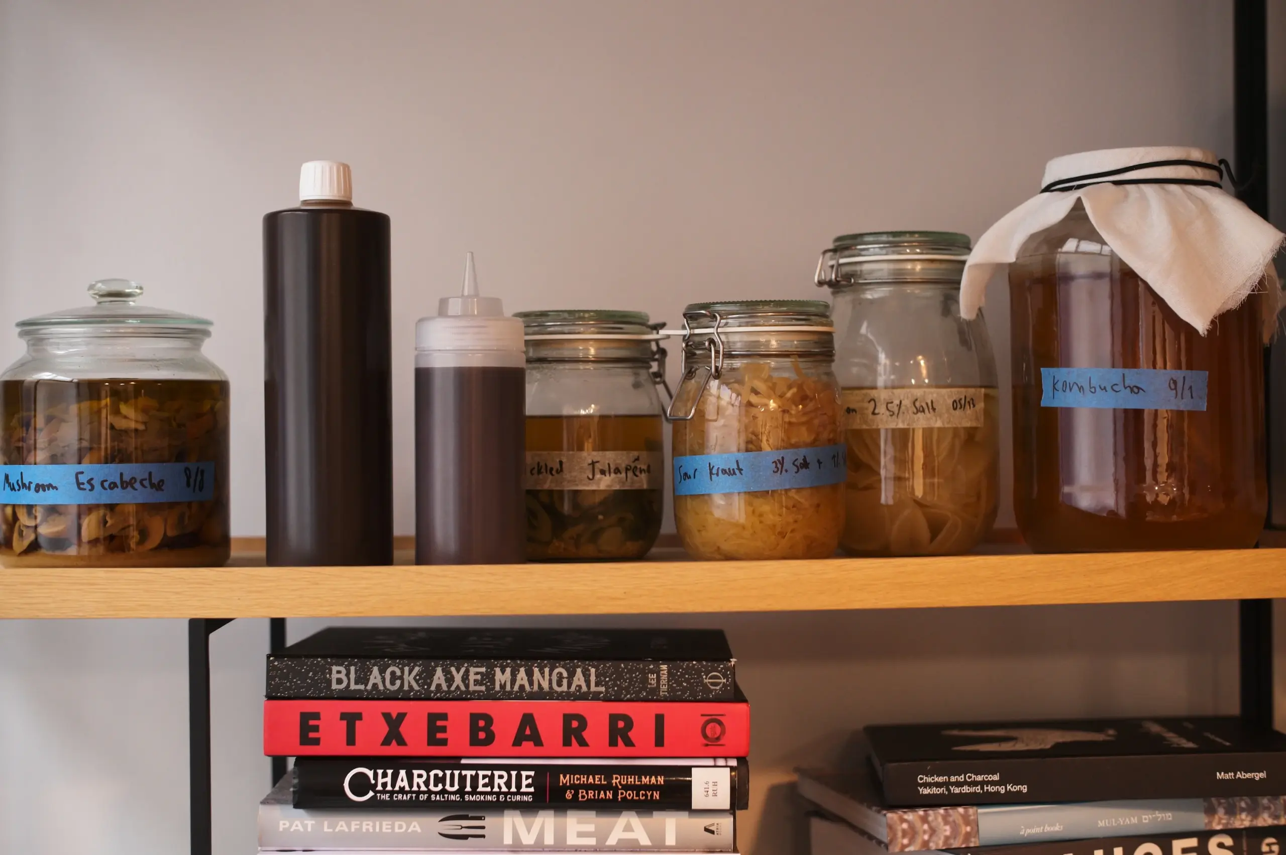 Glass jars with fermenting ingredients stored above culinary cookbooks.