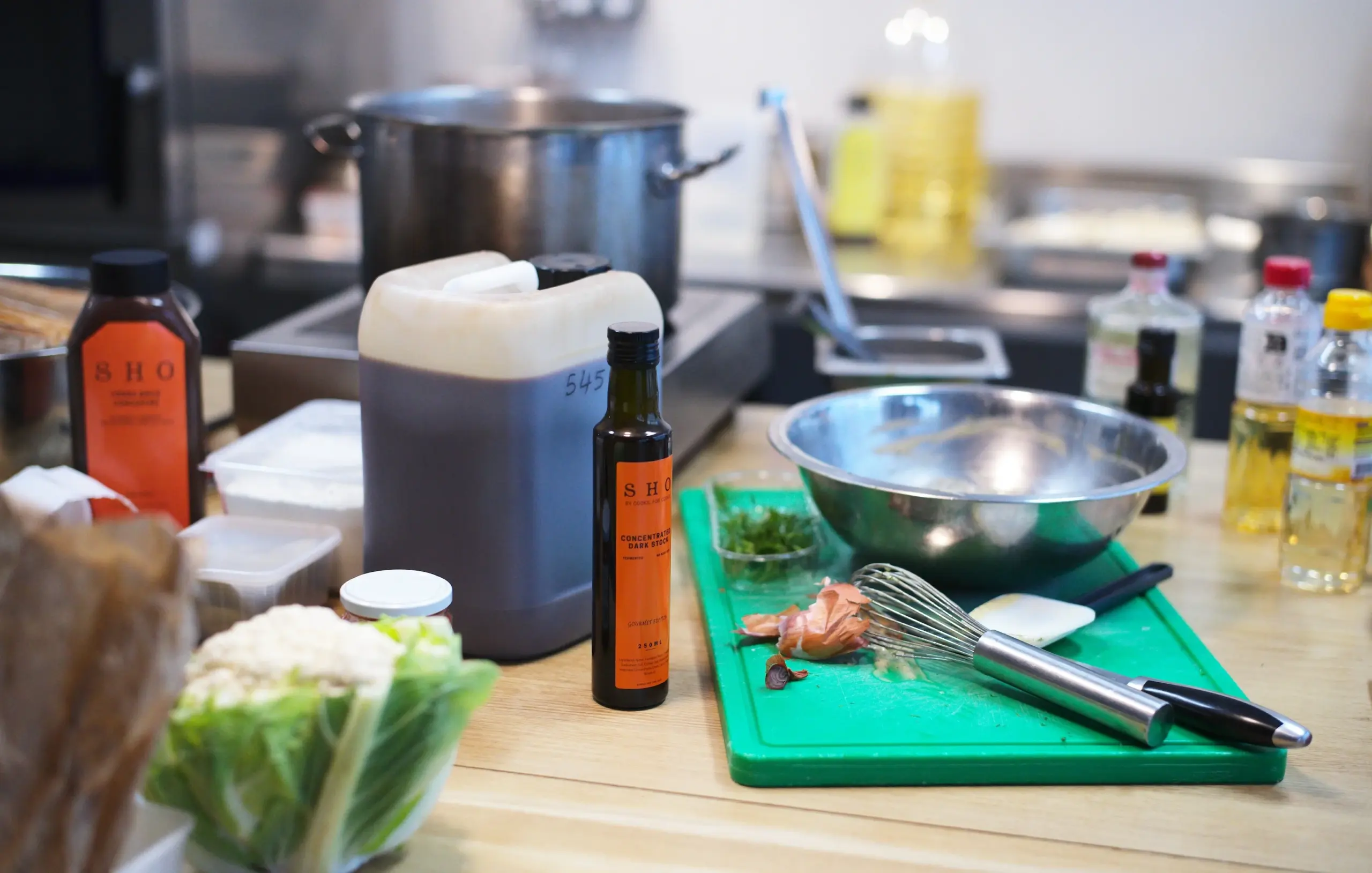 Fermented liquid sauces, oils, and fresh vegetables on a chef prep table.