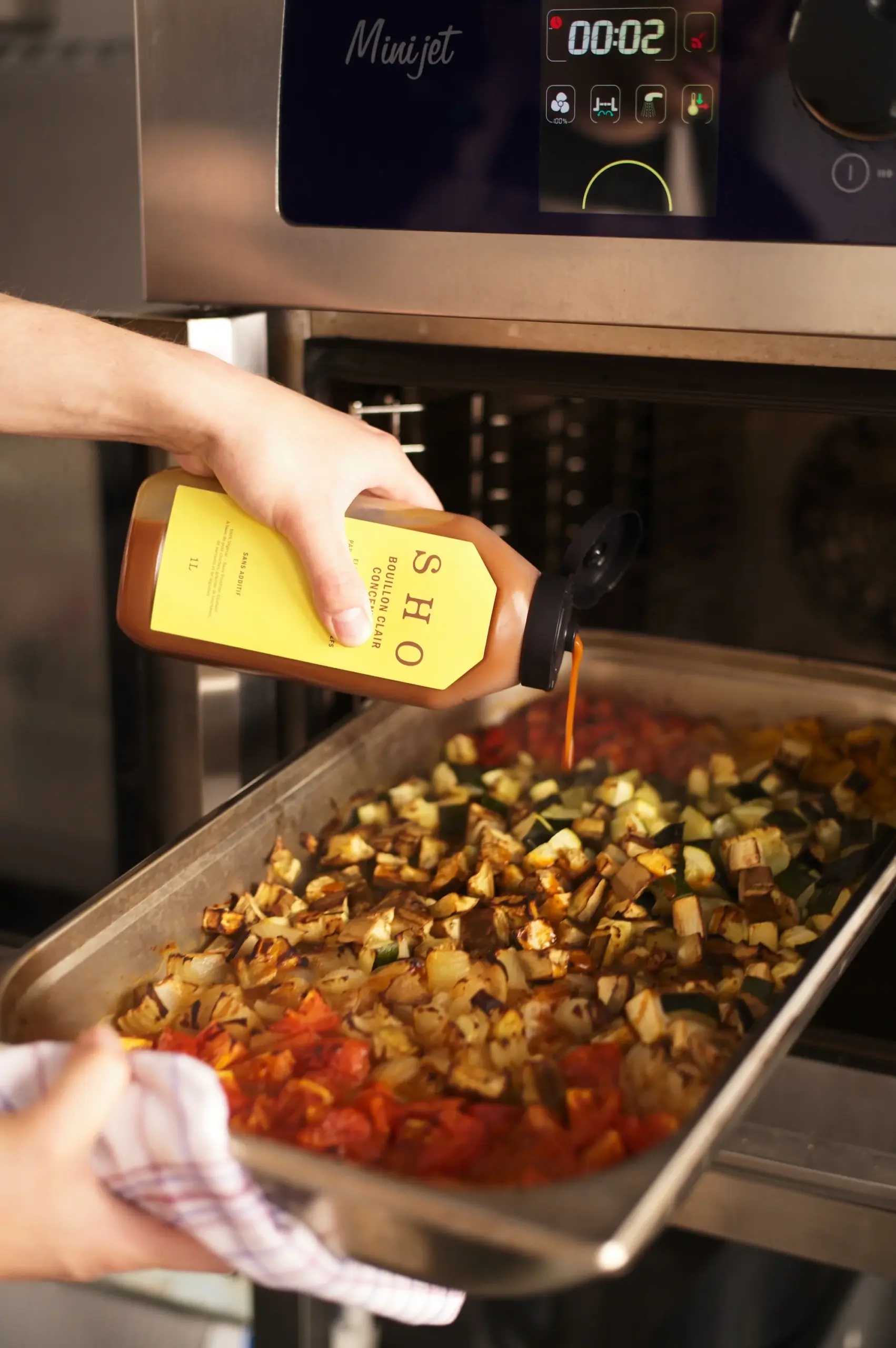 Pouring SHO fermented sauce onto a tray of roasted vegetables before oven cooking.