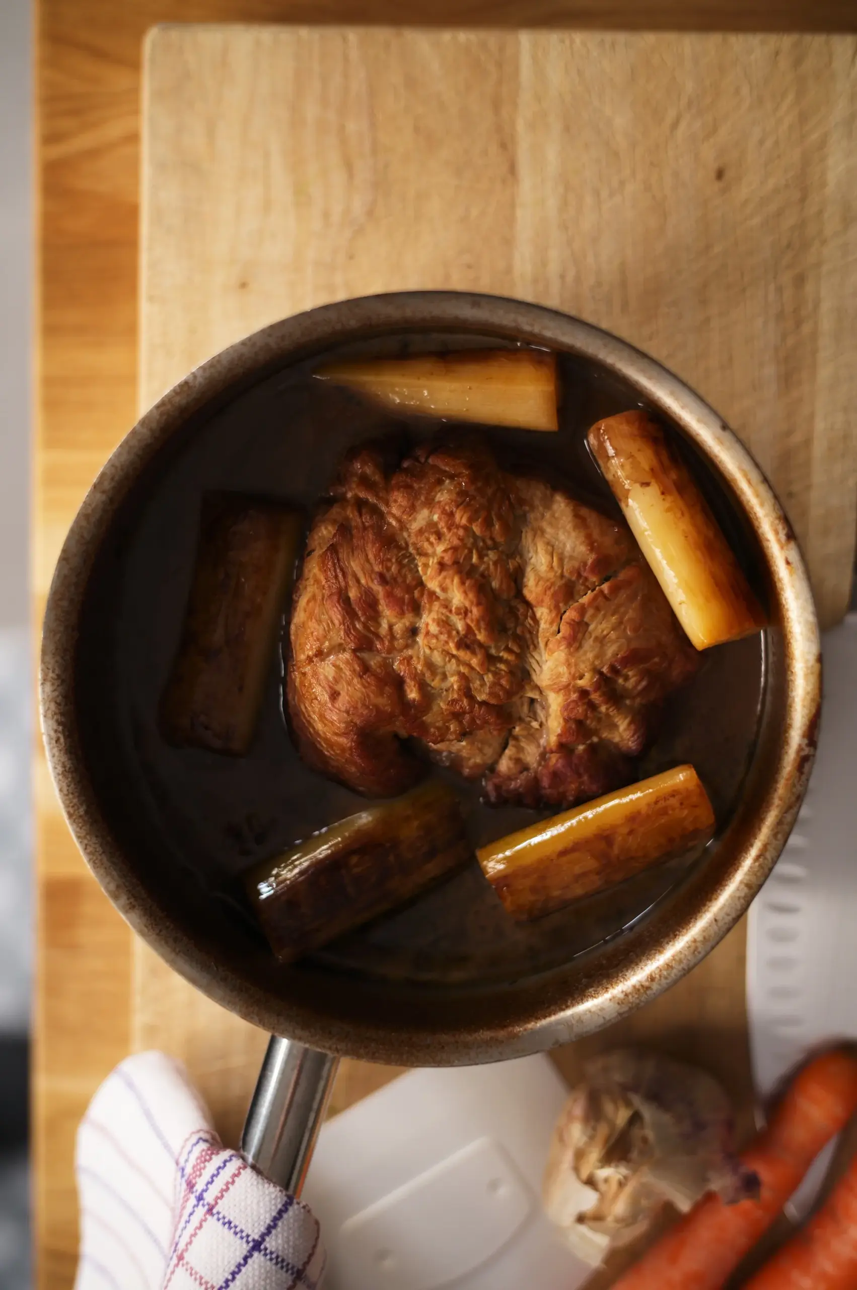 Slow-cooked beef piece with roasted carrots and leeks in a stainless steel pan.