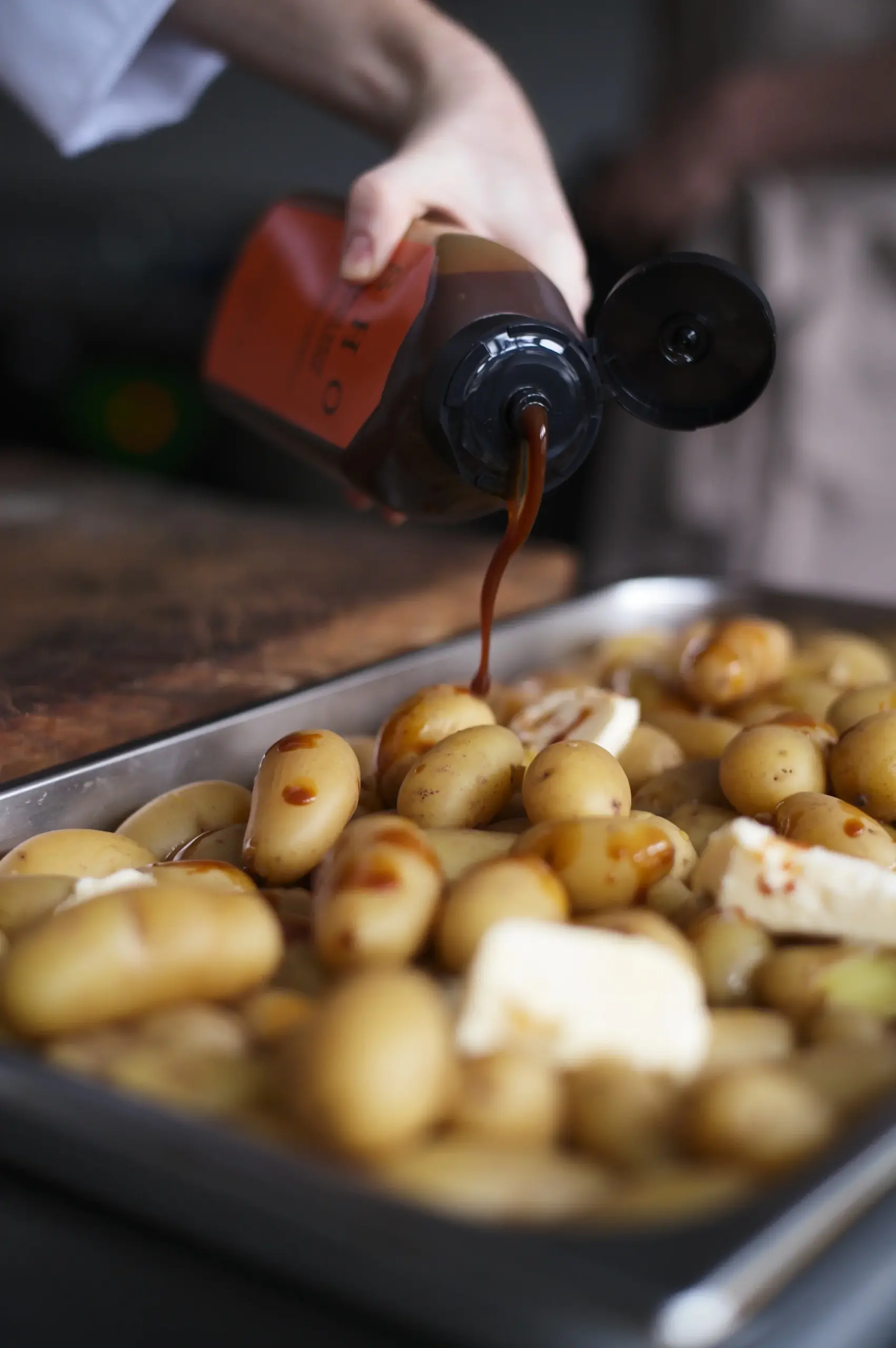 Squeezing a rich dark fermented sauce over buttered roasted baby potatoes on a tray.